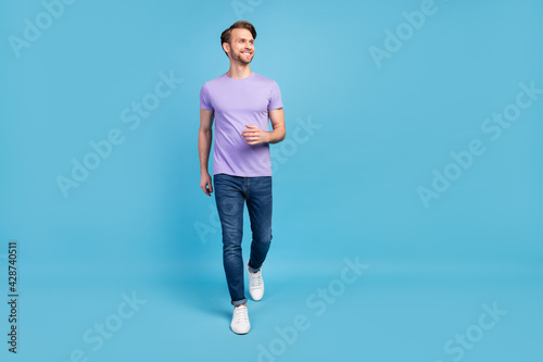 Full size portrait of positive person walking look interested empty space isolated on blue color background