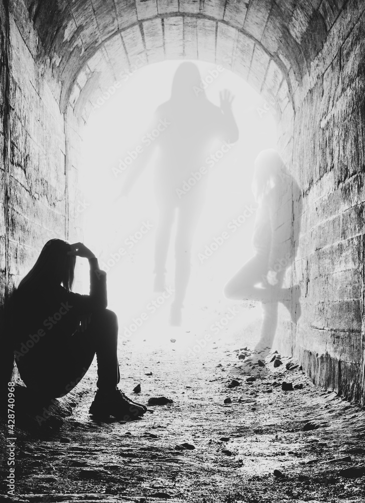 a dying young woman sits in a tunnel in bright rays of light. the soul of the girl opposite the body.