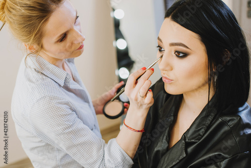 Makeup master doing makeup to beautiful model indoor beauty studio