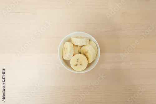 Fresh ripe organic sliced bananas in a ceramic bowl on a wooden table on top view