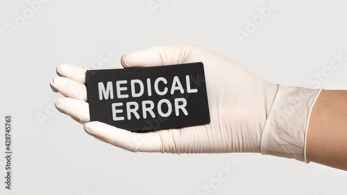 Closeup of the hand in a white sterile glove holding a card with text - medical error
