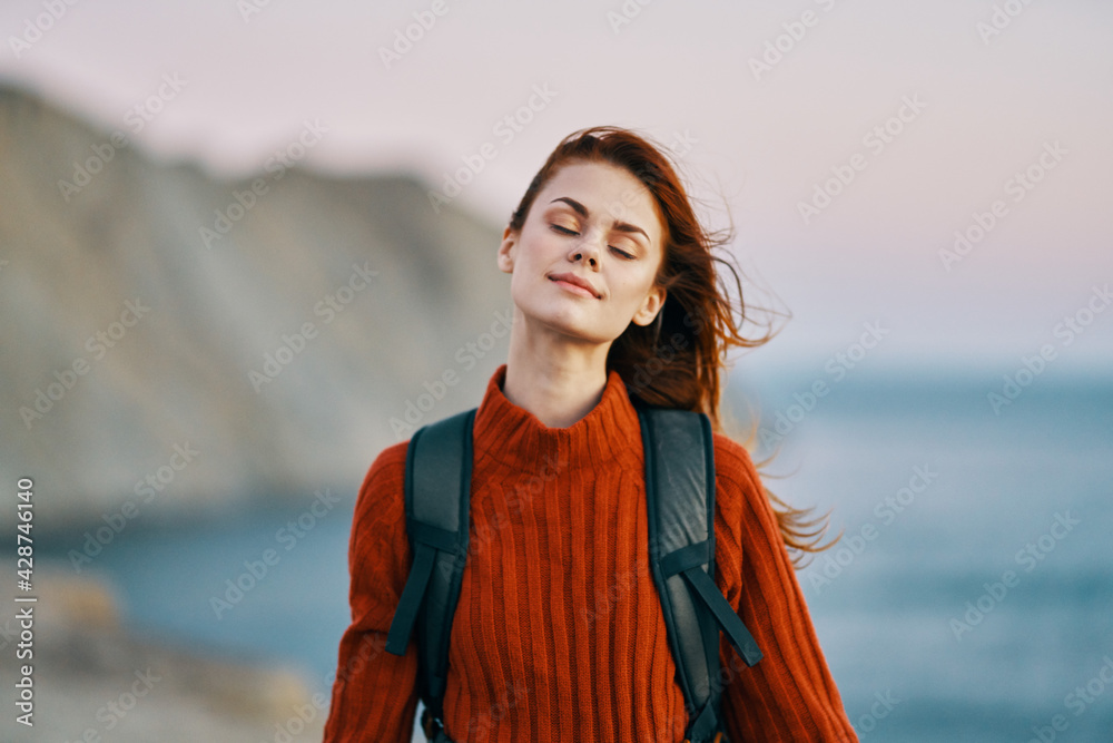 woman in a red sweater with a backpack on her back resting in the mountains outdoors near the ocean woman in a red sweater with a backpack on her back resting in the mountains outdoors near the ocean