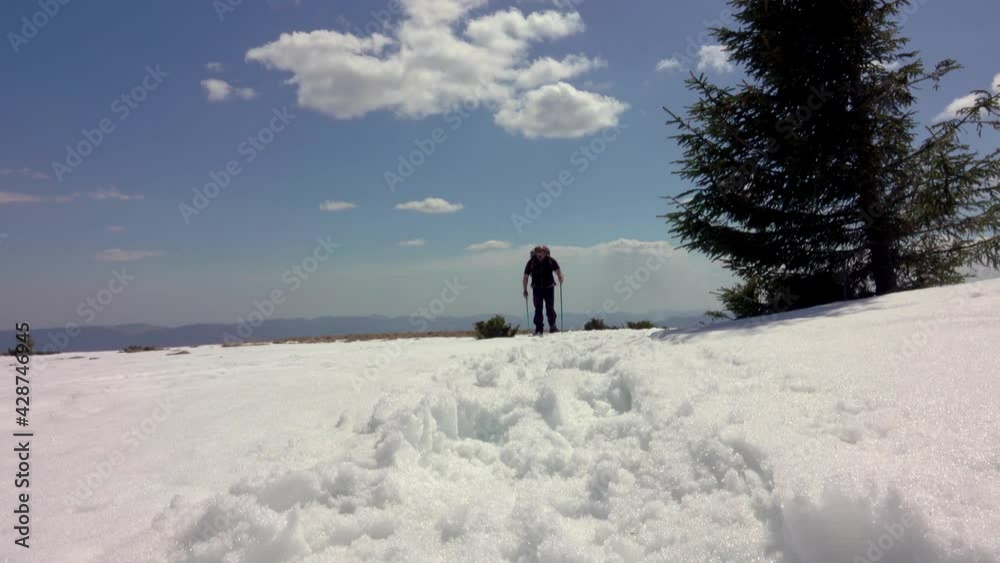Hiker Walking On A Mountain Ridge, with Snowshoes, Covered With Deep Snow. Winter Sunny Sky With Moving Clouds Hiker Walking On A Mountain Ridge, with Snowshoes, Covered With Deep Snow. Winter Sunny Sky With Moving Clouds