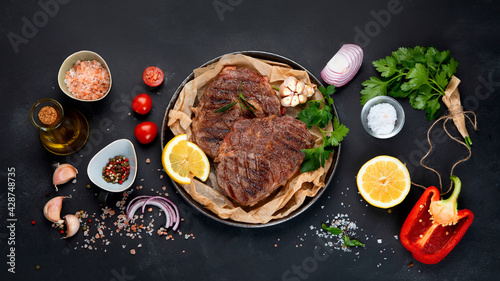 Delicious prepared meat steaks with seasoning and herbs on dark background.
