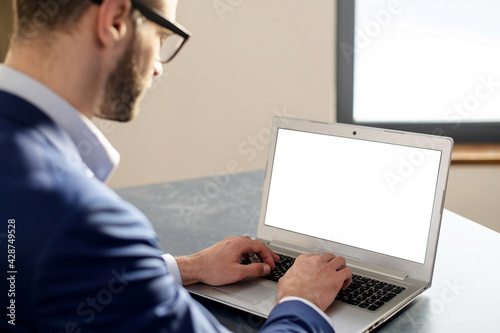 Over the shoulder photo of man sitting in front of a laptop, copy space, looking at something on the screen, choosing, viewing, texting, listening to lecture, using new modern fast communication app