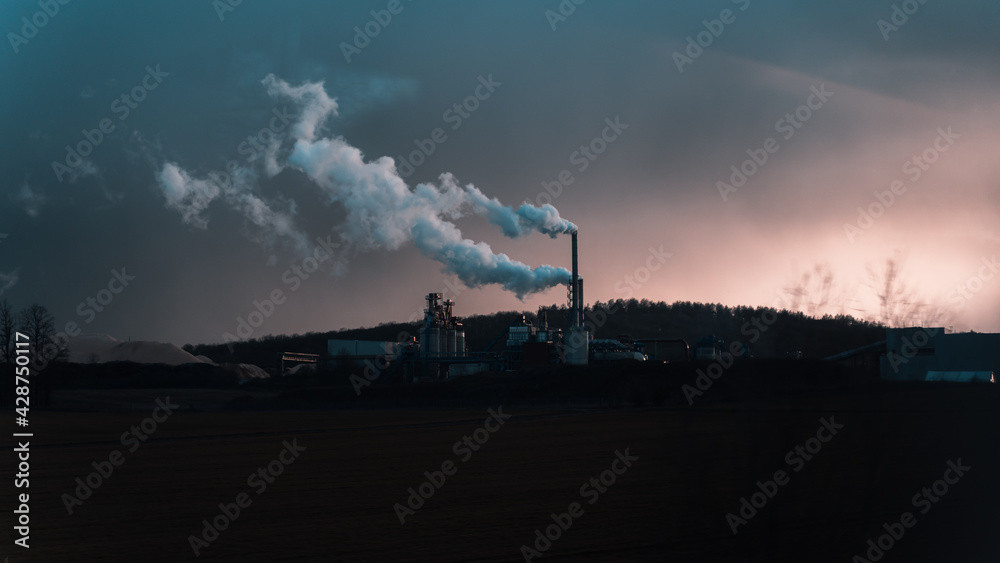 A factory at night with chimneys throwing out steam.