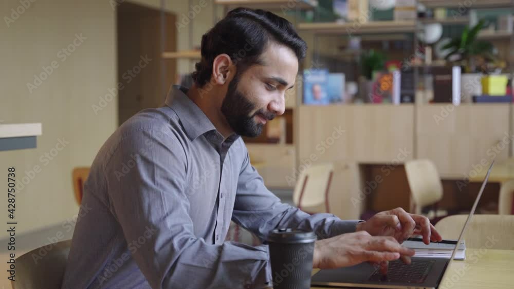 Happy bearded indian business man working on laptop from home office. Male indian executive using computer remote studying, browsing web, having virtual meeting, typing on computer.