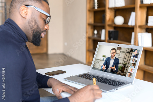 African man takes part in an online strategic meeting with mentor to build business or his brand  writing down in notebook ways of business development or problem solving  using fast convenient app