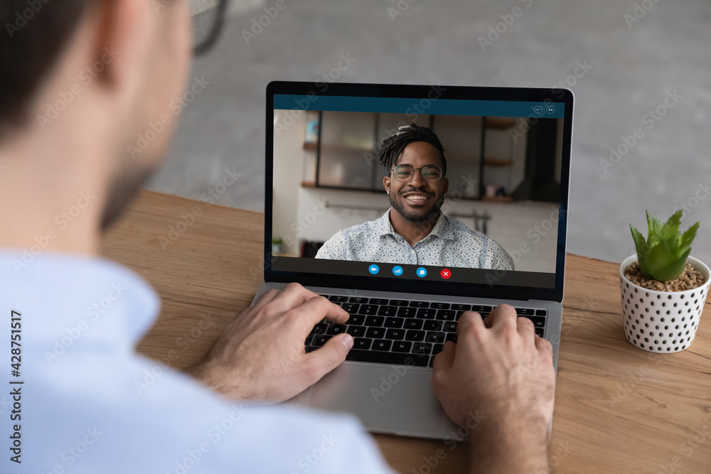 Close up back view of man use laptop talk on video call with smiling African American business partner or client. Colleagues have webcam digital zoom conference on compute. Virtual event concept. Close up back view of man use laptop talk on video call with smiling African American business partner or client. Colleagues have webcam digital zoom conference on compute. Virtual event concept.