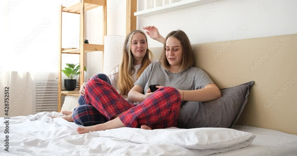 Young lesbian couple using smartphone together, sitting on bed Young lesbian couple using smartphone together, sitting on bed