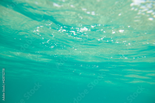 Turquoise calm sea with waves and rays of sunlight shining through, underwater. Ocean. Tranquility and silence. Beautiful natural background, wallpaper