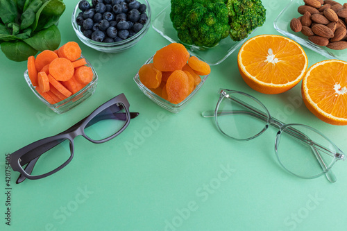 Two glasses and products for improving vision, spinach, dried apricots, blueberries, orange, almonds and broccoli on a green background. photo