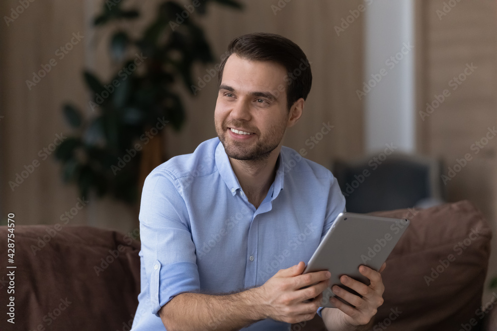 Happy millennial man relax at home use modern tablet gadget look in distance thinking planning. Smiling young Caucasian male hold pad device make decision. Technology, communication concept. Happy millennial man relax at home use modern tablet gadget look in distance thinking planning. Smiling young Caucasian male hold pad device make decision. Technology, communication concept.