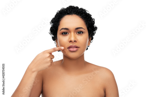 beauty, aesthetic surgery and people concept - portrait of happy smiling young african american woman with bare shoulders pointing to her lips over white background