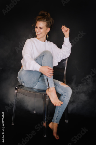 Portrait Frau, kraftvoll, Fitness, dunkler Hintergrund, zerissene Jeans auf Sessel, weißer Pulli, Bauchfrei