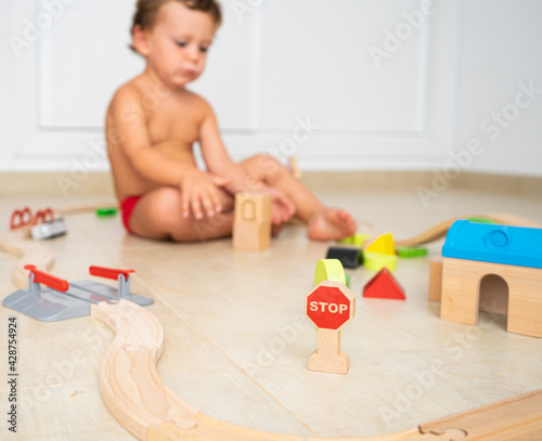 Child playing with wooden toys on the floor of his room, in summer.