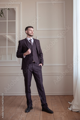 beautiful young man with a beard brunette model. guy in a classic suit in a light stylish interior. © fasli