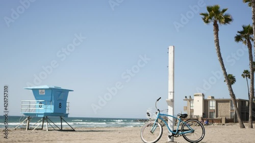 Blue bicycle, cruiser bike by ocean beach, pacific coast, Oceanside California USA. Summertime vacations, sea shore. Vintage cycle on sand near lifeguard tower or watchtower hut. Sky and water waves.