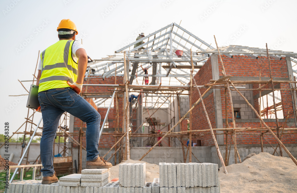 Engineering Consulting People on construction site holding notebook computer in his hand. Home building inspector. Construction site check drawing and business workflow of new structure building Engineering Consulting People on construction site holding notebook computer in his hand. Home building inspector. Construction site check drawing and business workflow of new structure building