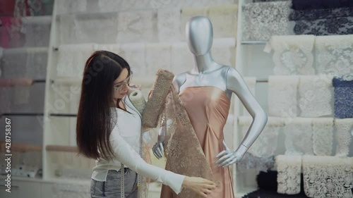 Fashion and tailoring concept. Professional brunette dressmaker, designer or seamstress working with new model applying textile cloth on mannequin or dummy in atelier or studio. 4k footage