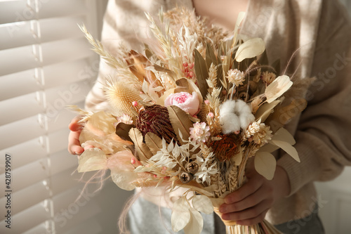 Woman holding beautiful dried flower bouquet near window at home, closeup © New Africa