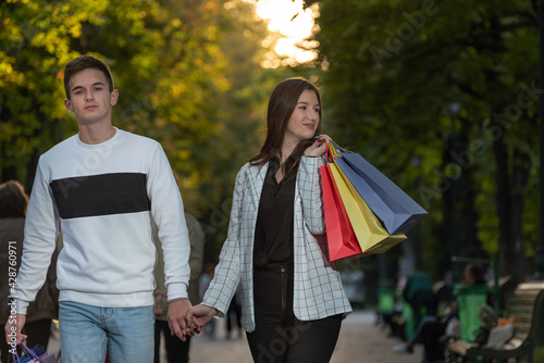 Young couple in love walking in park. Happy girl holding shopping bags