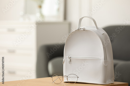 Stylish white backpack and glasses on wooden table indoors, space for text