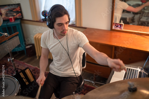 Young man with headphones plays drums in home music room