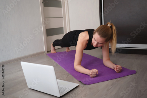 young woman doing asana at home on yoga mat in front of laptop