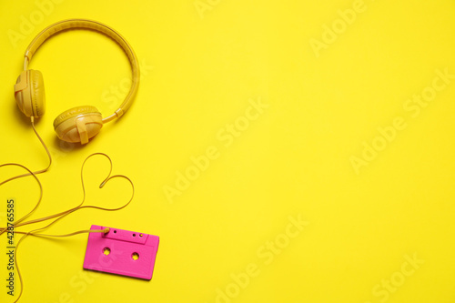 Heart made with cable of headphones and music cassette on yellow background, flat lay. Space for text