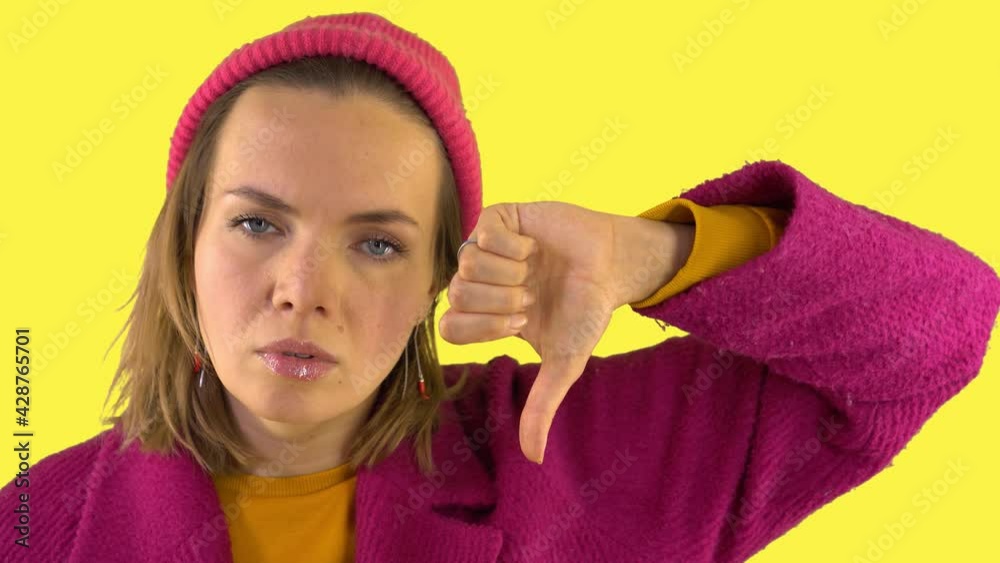 Displeased woman in red coat and hat shows thumbs down. Sad hand gesture. Emotions of failure. Serious facial expression. Yellow background, studio video, 4K, portrait. Displeased woman in red coat and hat shows thumbs down. Sad hand gesture. Emotions of failure. Serious facial expression. Yellow background, studio video, 4K, portrait.