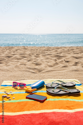 Towel, sunscreen, flip-flops, sunglasses and smart phone on the beach. Summer concept.