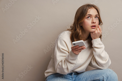 Photos Young puzzled woman using mobile phone while sitting