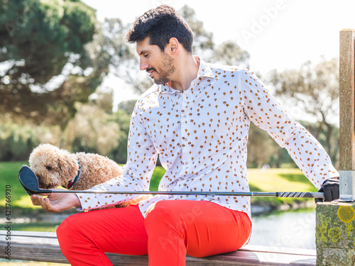 A young Caucasian male playing with his Goldendoodle dog on a professional golf course