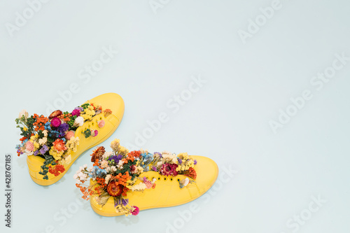 Yellow sneakers on a pastel blue background filled with flowers. Spring minimal modern koncept. 