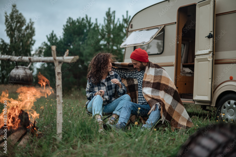 Obraz premium Couple in a checkered plaid roasting marshmallows on fire near the trailer home.