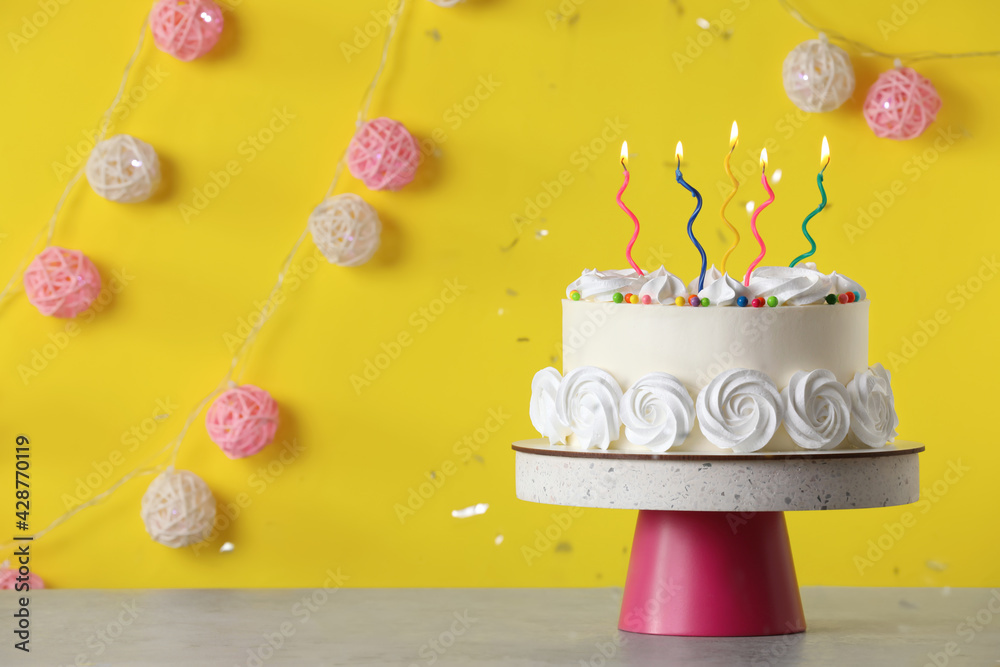 Birthday cake with burning candles on table near yellow wall, space for text - obrazy, fototapety, plakaty 