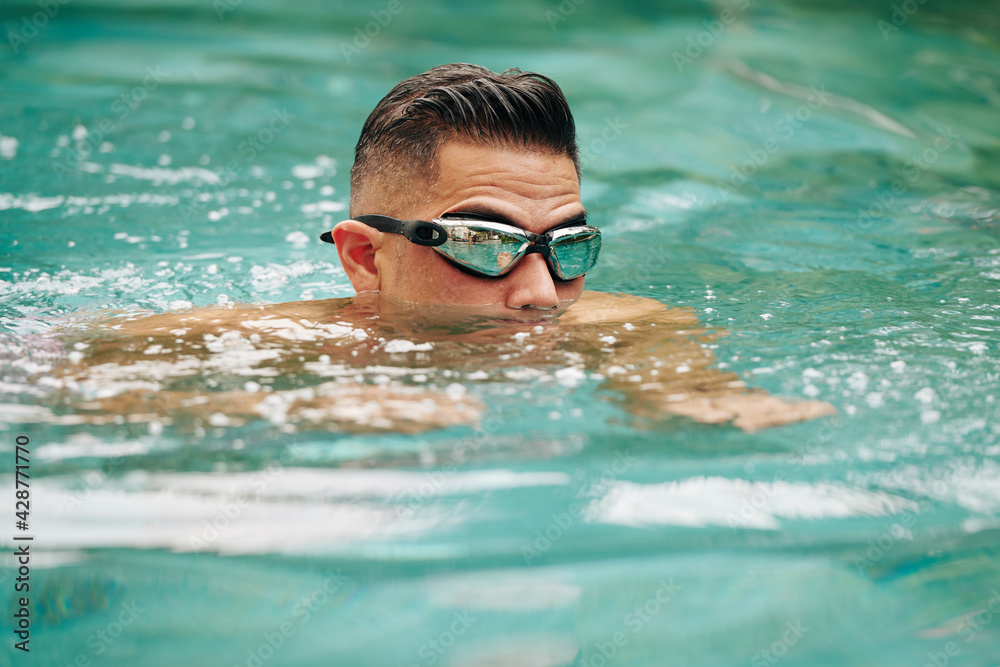 Man in mirrored goggles swimming breaststroke in outdoor pool