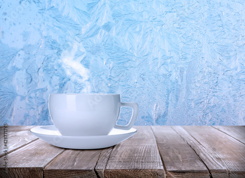 Cup of hot tea on table near window covered with frost