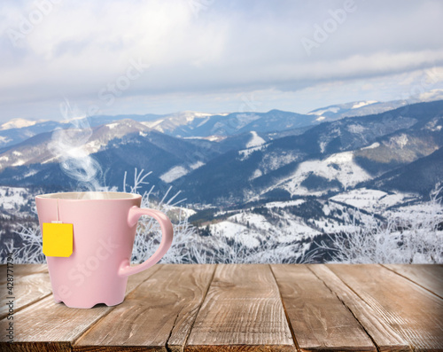 Cup of hot tea on wooden table and beautiful winter landscape on background © New Africa