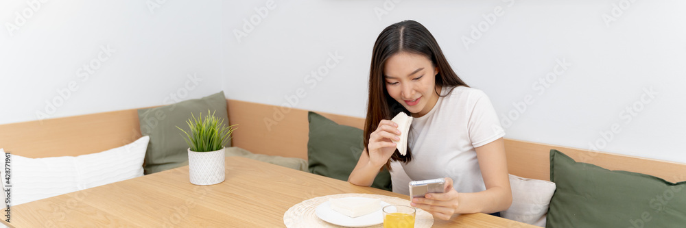 Happy asian woman using mobile phone during breakfast. or eating lunch while working from home. Happy asian woman using mobile phone during breakfast. or eating lunch while working from home.