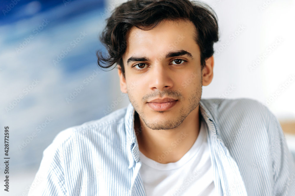 Close up portrait of a charismatic handsome confident mixed race hispanic guy, wearing blue shirt, looking directly at the camera with friendly smile Close up portrait of a charismatic handsome confident mixed race hispanic guy, wearing blue shirt, looking directly at the camera with friendly smile