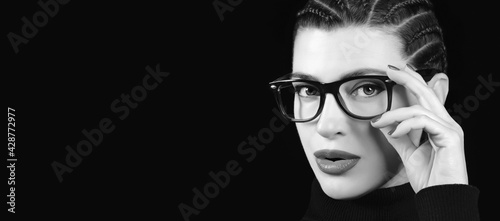 Monochrome young woman with braided hair wearing eyeglasses. Vision care, optometry and fashion eye wear concept isolated on black background