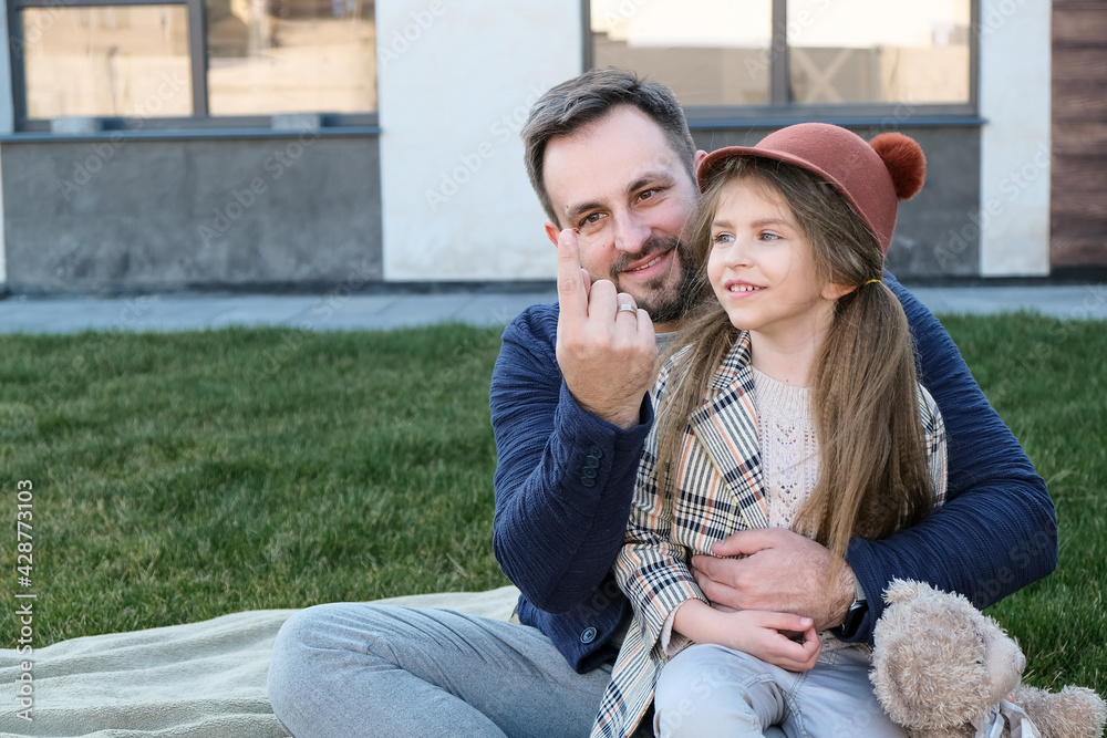 Father and daughter sitting together on the grass on the backyard of their house looking at the lady bug on dad's finger and smiling, father's day