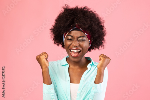 Emotional Bushy Black Woman Shaking Fists Celebrating Success, Pink Background