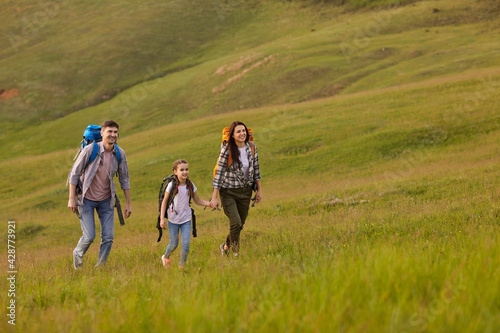 Happy family with backpacks travel through the hills in the countryside in summer.