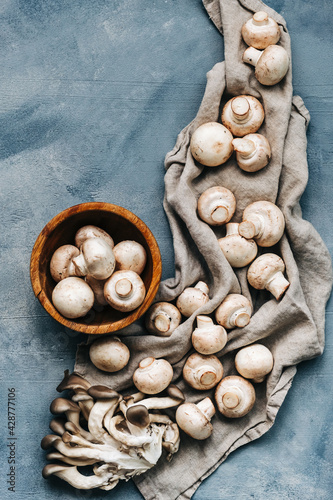 Fresh mushrooms champignons and oyster mushrooms with linen fabric cloth on blue table in kitchen, top view.