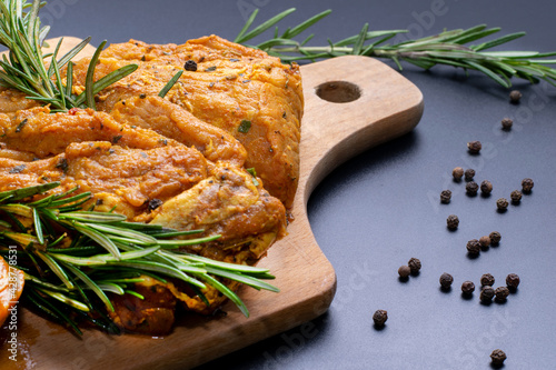 Raw marinated meat, steaks with rosemary and pepper on a black background