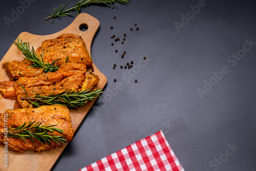 Raw marinated meat, steaks with rosemary and pepper on a black background