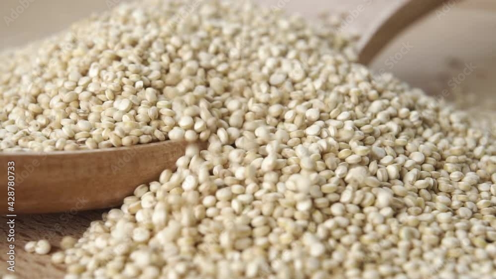 Pouring raw quinoa seeds into a wooden spoon in slow motion. Macro shot. Super food concept Pouring raw quinoa seeds into a wooden spoon in slow motion. Macro shot. Super food concept